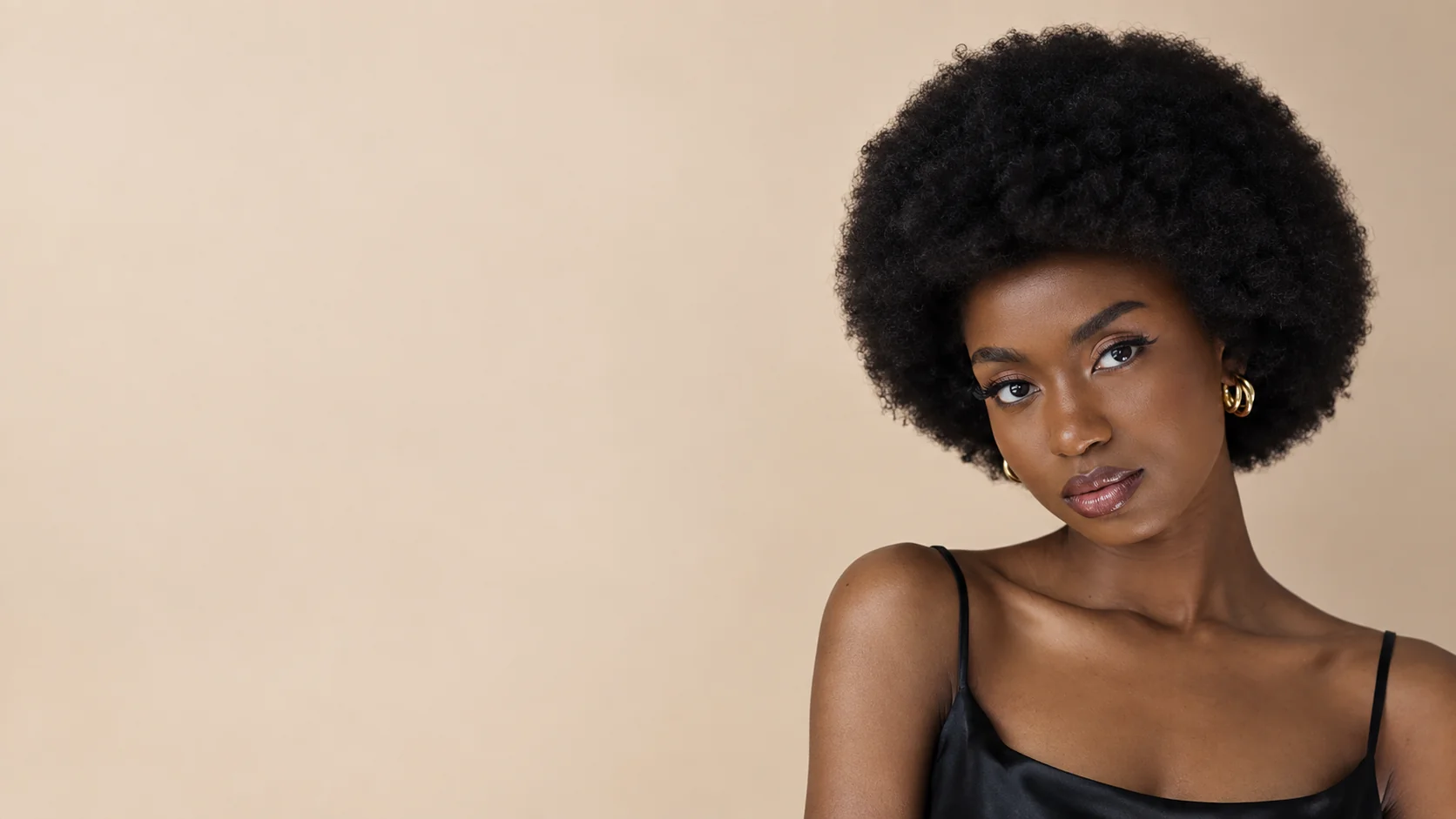 Woman with a full natural afro, radiant skin and gold hoop earrings, looking at the camera